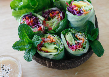 fresh spring rolls filled with colorful veggies in a black bowl with a sprig of mint