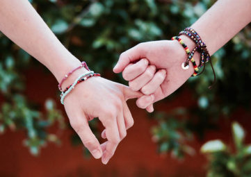 Two preteen hands with beaded bracelets on "holding pinkies"