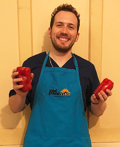 Volunteer in teal apron holding up two red bell peppers