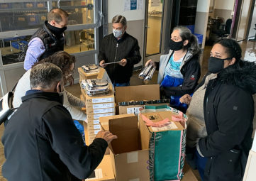 Three women and three men wearing masks, sorting and organizing boxes of donated headsets and other tech items