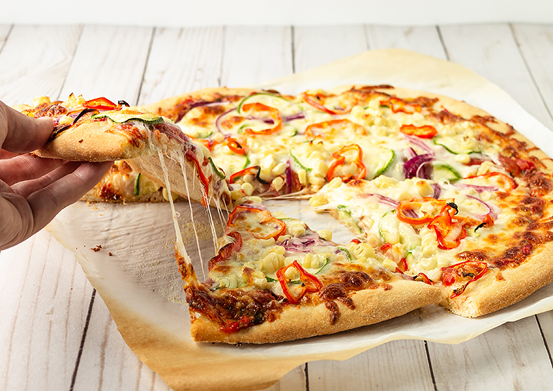 Hand picks up a slice from a freshly baked veggie pizza, with cheese stretching