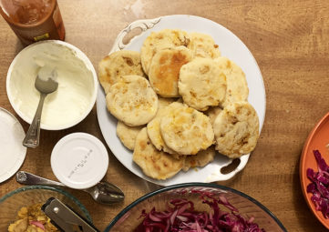 Pupusas on a white plate next to a plate of red cabbage slaw and other condiments