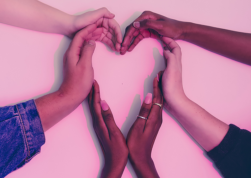 Six hands of people of different skin tones making a heart shape on a light-pink background