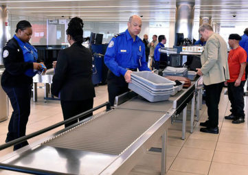 Two TSA in royal blue shirts work at the baggage security area