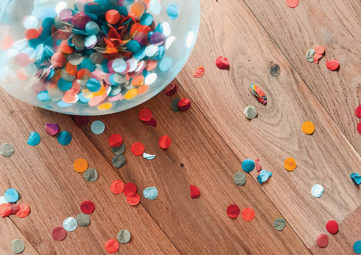 Colorful bowl of confetti on a wooden table strewn with confetti