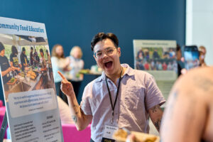 A person opens their mouth wide while pointing to a poster that says "Community Food Education."