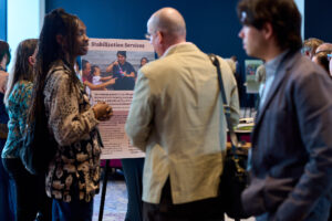 Two people talk in front of a poster showing a family playing with bubbles below the words "Stabilization Services."