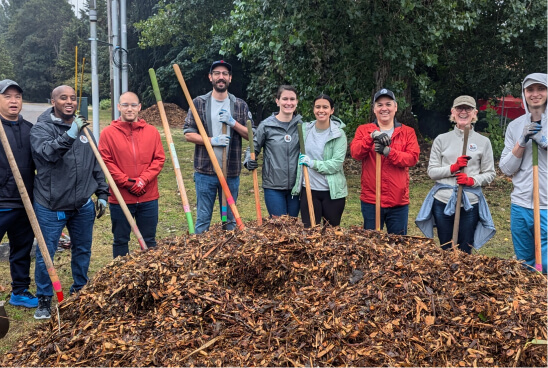 Volunteers pose with shovels behind a pile of mulch.