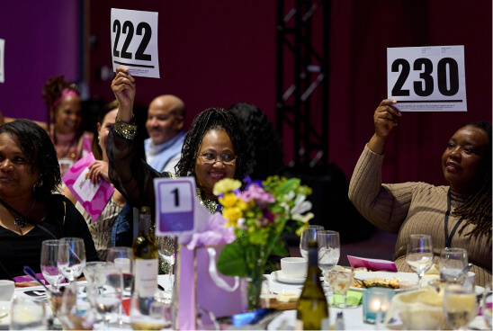 Bidders at a fancy dinner event hold up their numbers and smile.