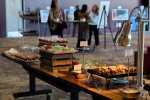 A selection of hors d'oeuvres on a long table at a reception with blurry people talking in the background.