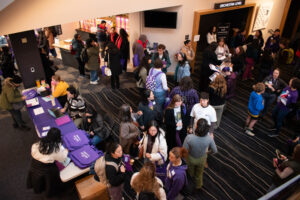 An overhead shot of a hallway outside a door labeled "orchestra level" crowded with people chatting in groups.