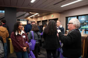 People mill about in a room with windows facing a street.