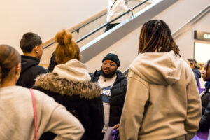 A man stands in front of a staircase as others face him.