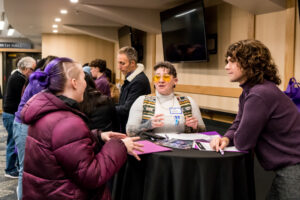 A person in amber-colored glasses speaks as two others listen.