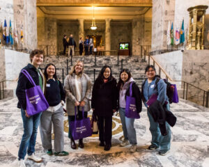 A group of people pose for a photo in front of a marble staircase in what appears to be a government building.