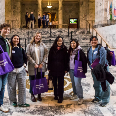 A group of people pose for a photo in front of a marble staircase in what appears to be a government building.