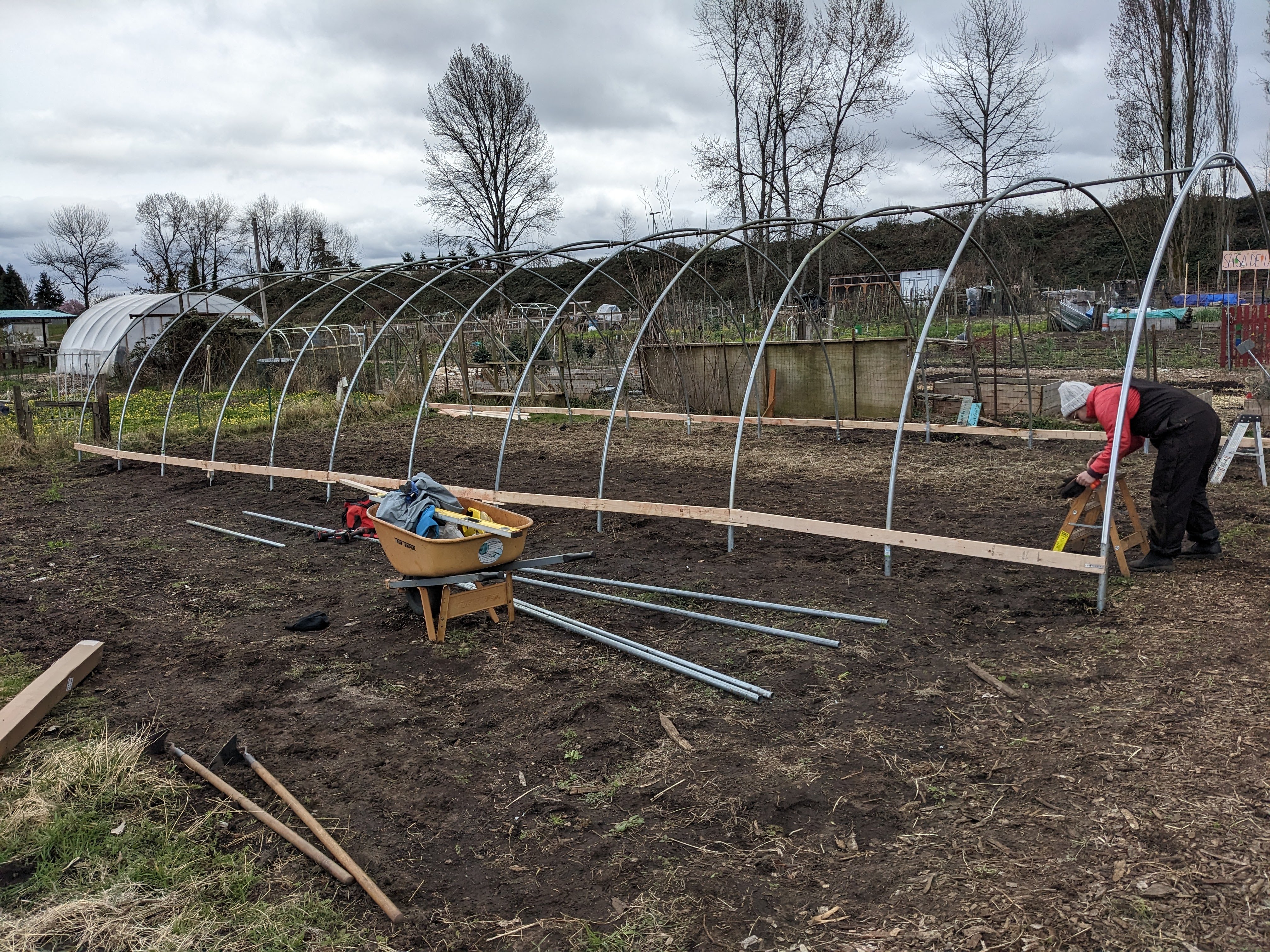 A person in a knit hat and overalls works under a series of arched pipes on a farm.