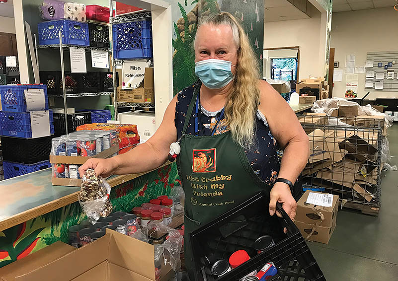 Woman with long blonde hair in a mask and apron crates food in a food pantry