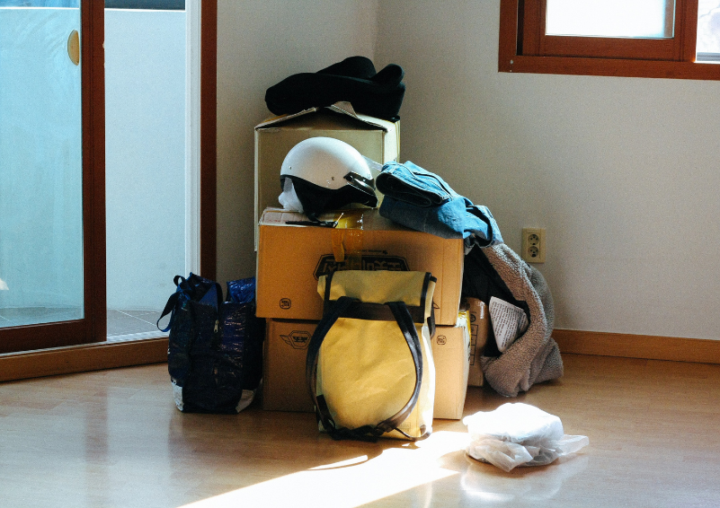 Moving boxes and backpacks stacked in the corner of a room.