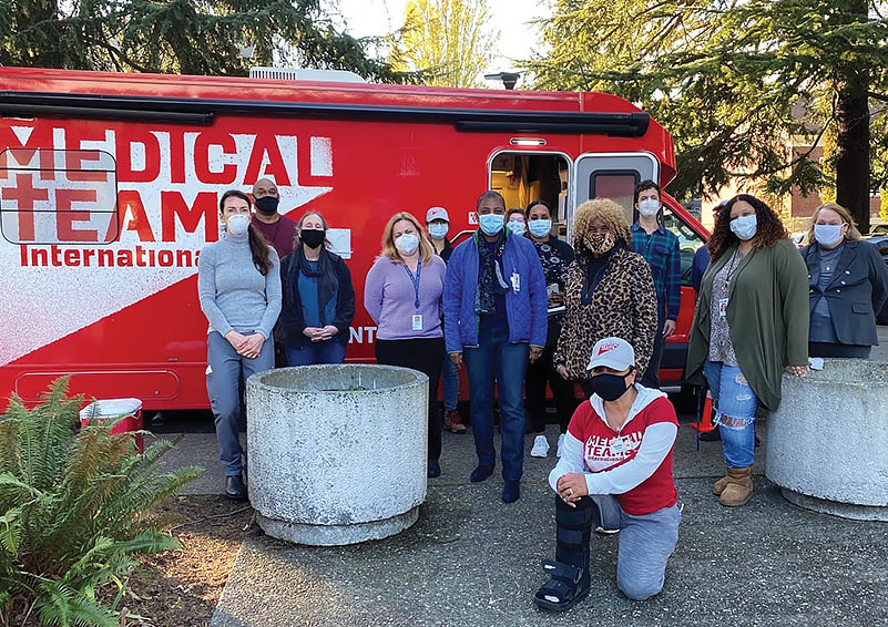 Group of people wearing masks pose in from of a red and white mobile COVID-19 testing van.