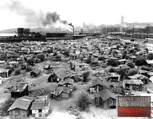 Black and white photo of shacks in downtown Seattle, with a smokestack and Smith Tower in the background, marked with "Hooverville U.S. Mail Charles St." in the bottom right corner
