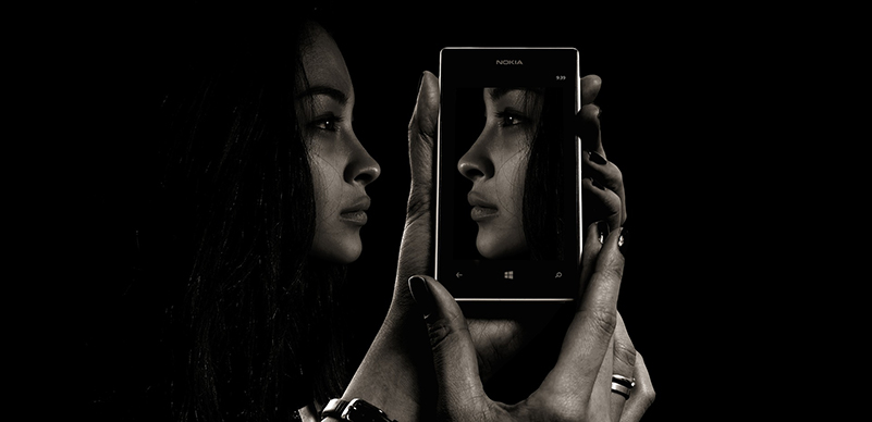 Black and white image of a woman's face reflected in her cellphone