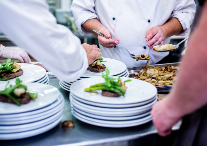 Three people in white kitchen coats carefully arrange food on shite plates