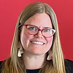 Headshot of a smiling white woman with blonde hair, red-framed glasses, and a black top with a red background