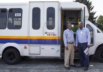 Two Solid Ground Transportation drivers standing by the open door of a paratransit van.