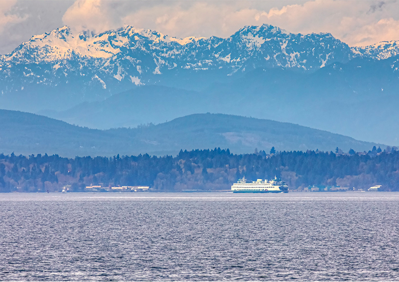 A ferry boat on purple Puget Sound waters with blue, snow-capped Cascade Mountains in the distance.