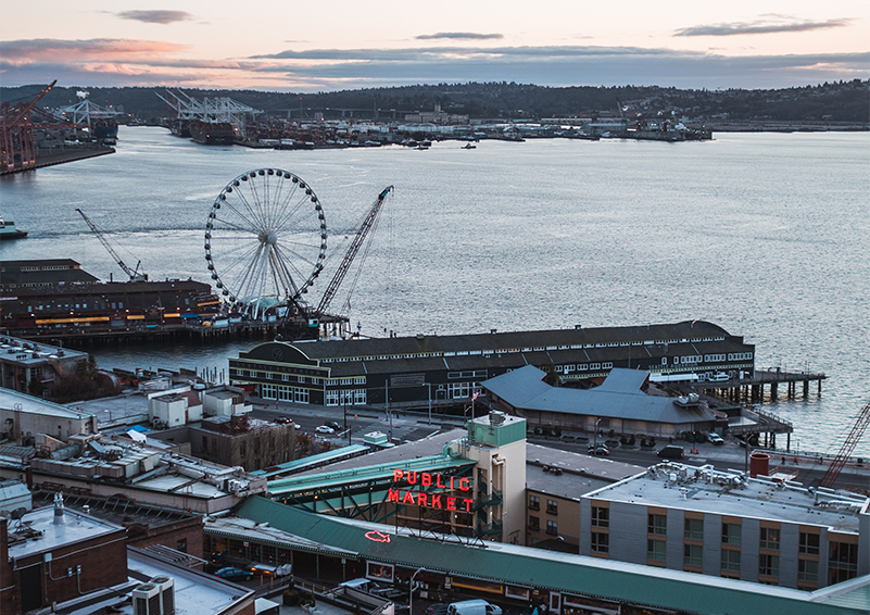 A view of Pike Place Market, the Seattle Wheel and Elliot Bay at dusk.