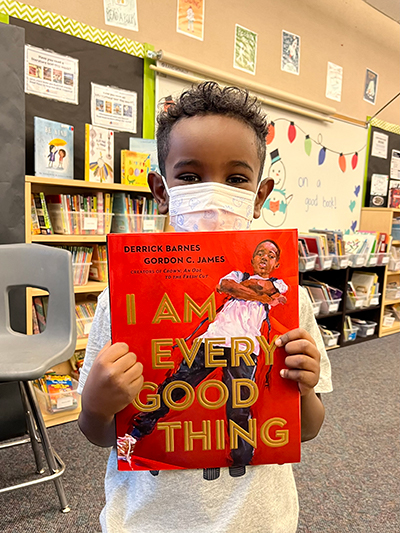 A young boy holding a book titled, "I am every good thing."