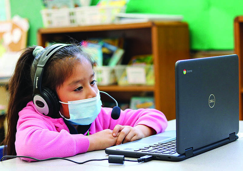 A young girl in a pink shirt watches a laptop while wearing a headset.