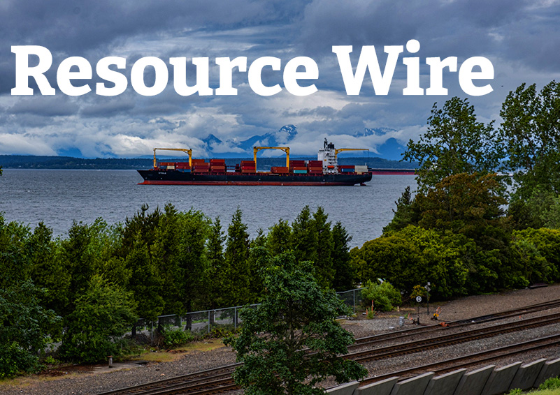 A large containers ship floats in Puget Sound with railroad tracks and trees in the foreground and a gray, cloudy sky above. The words "Resource Wire" are embossed in the clouds.