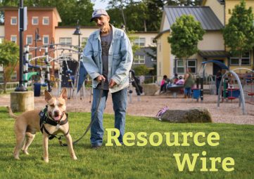 A man in a jean jacket with his dog on a leash on the grass in front of a playground, with the words "Resource Wire" embossed over the grass.