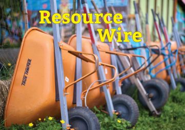A series of orange and blue wheelbarrows leaning up against a fence with the words "Resource Wire" above them