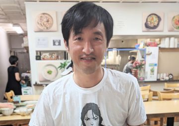 A man with dark hair and white t-shirt with a restaurant scene in the background