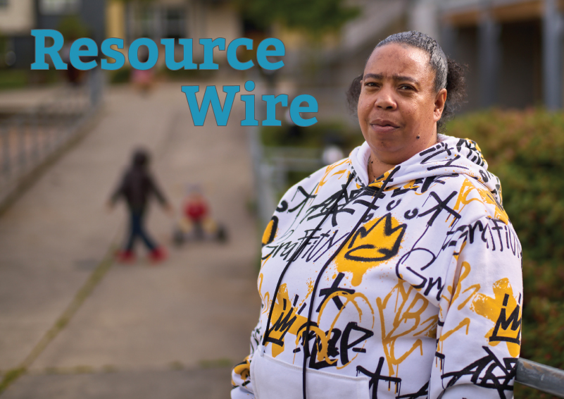 A woman standing on a sidewalk in a white hoodie with gold and black graffiti-style writing on it. A child, out of focus, plays in the background. The words "Resource Wire" appear on the image.