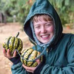 A woman in a green hoodie holds to yellow and green winter squashes.