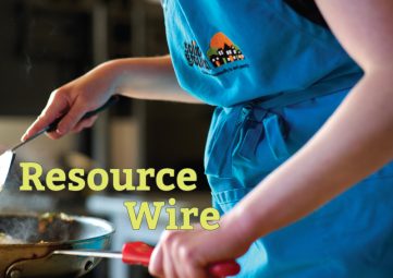 A close-up shot of someone in a blue apron with one hand on the handle of a frying pan and the other hand stirring something with a spatula. The words "Resource Wire" appear on the image.
