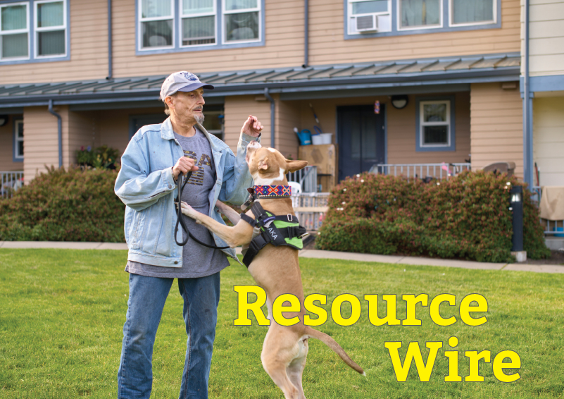 A man in a jeans jacket and hat plays with his dog. There's an apartment building in the background and the words "Resource Wire" in the foreground.