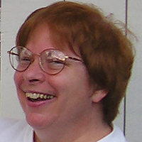 A smiling woman with radish hair and glasses.