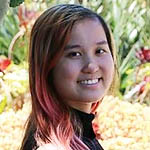 Headshot of a young Asian woman outdoors. She has reddish hair and is wearing a black turtleneck.