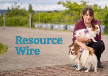 A woman wearing a cranberry-colored sweater crouches down a small dog on her lap and another infront of her. The words "Resource Wire" appear besides her.