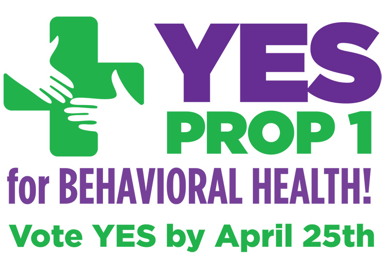 A campaign sign with green and purple letters over a white background that read "Yes Prop 1 for behavioral health. Vote YES by April 25th."