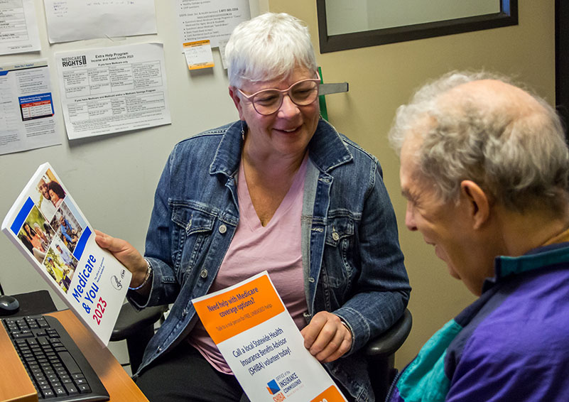 Two gray-haired adults talking to each other while holding Medicare brochures.