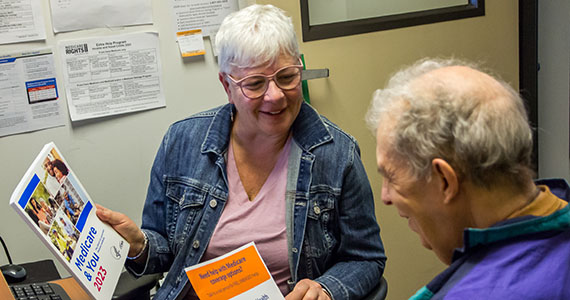 Two gray-haired adults talking to each other while holding Medicare brochures.