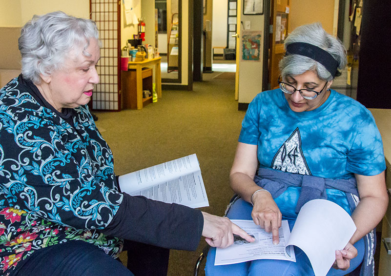 Two gray-haired women holding Medicare materials while discussing them.