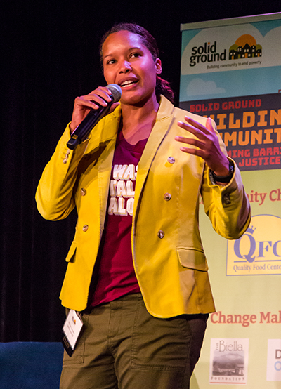 A woman holding a microphone and wearing a yellow sports coat
