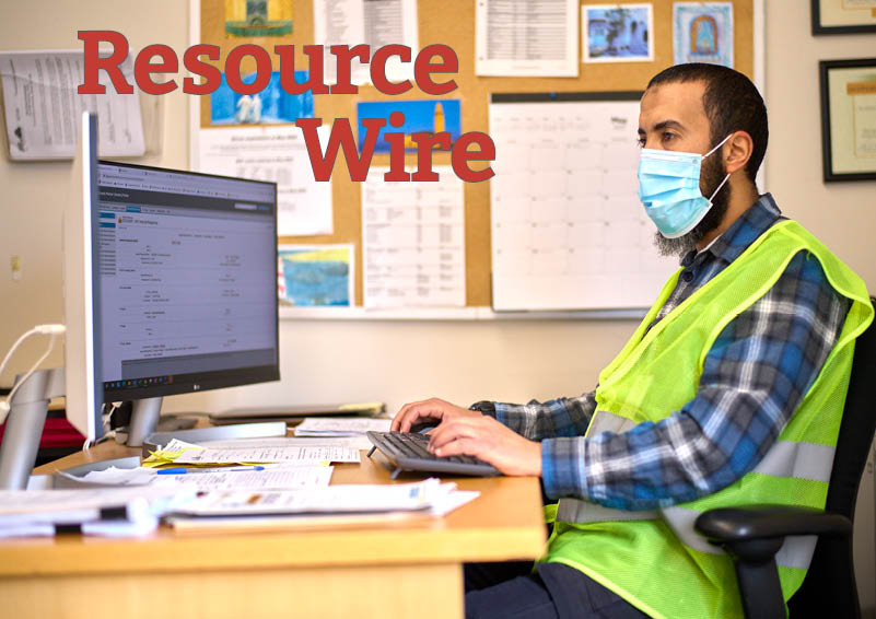 A man wearing a surgical mask and bright neon vest sits at a computer in an office. The words "Resource Wire" appear on the image.